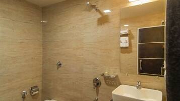A bathroom with a toilet, sink, shower, and a trash bin.