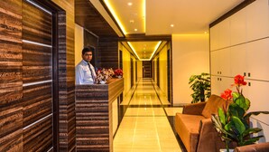 A modern hotel lobby with a long reception desk, a brown leather sofa, and a potted plant. - Rudra Shelter International (Vasai)
