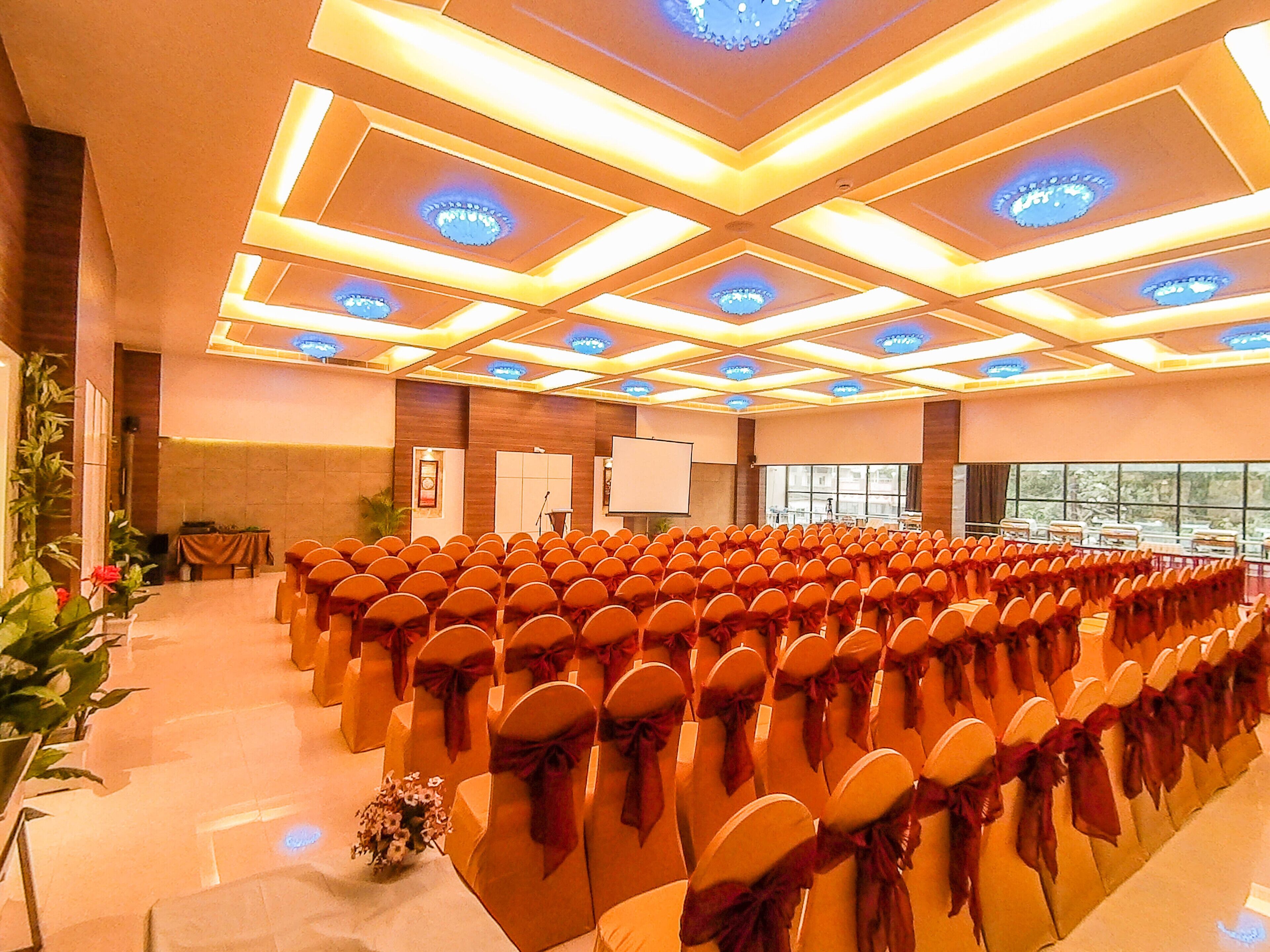 A conference room with rows of chairs, a podium, and a large screen.
