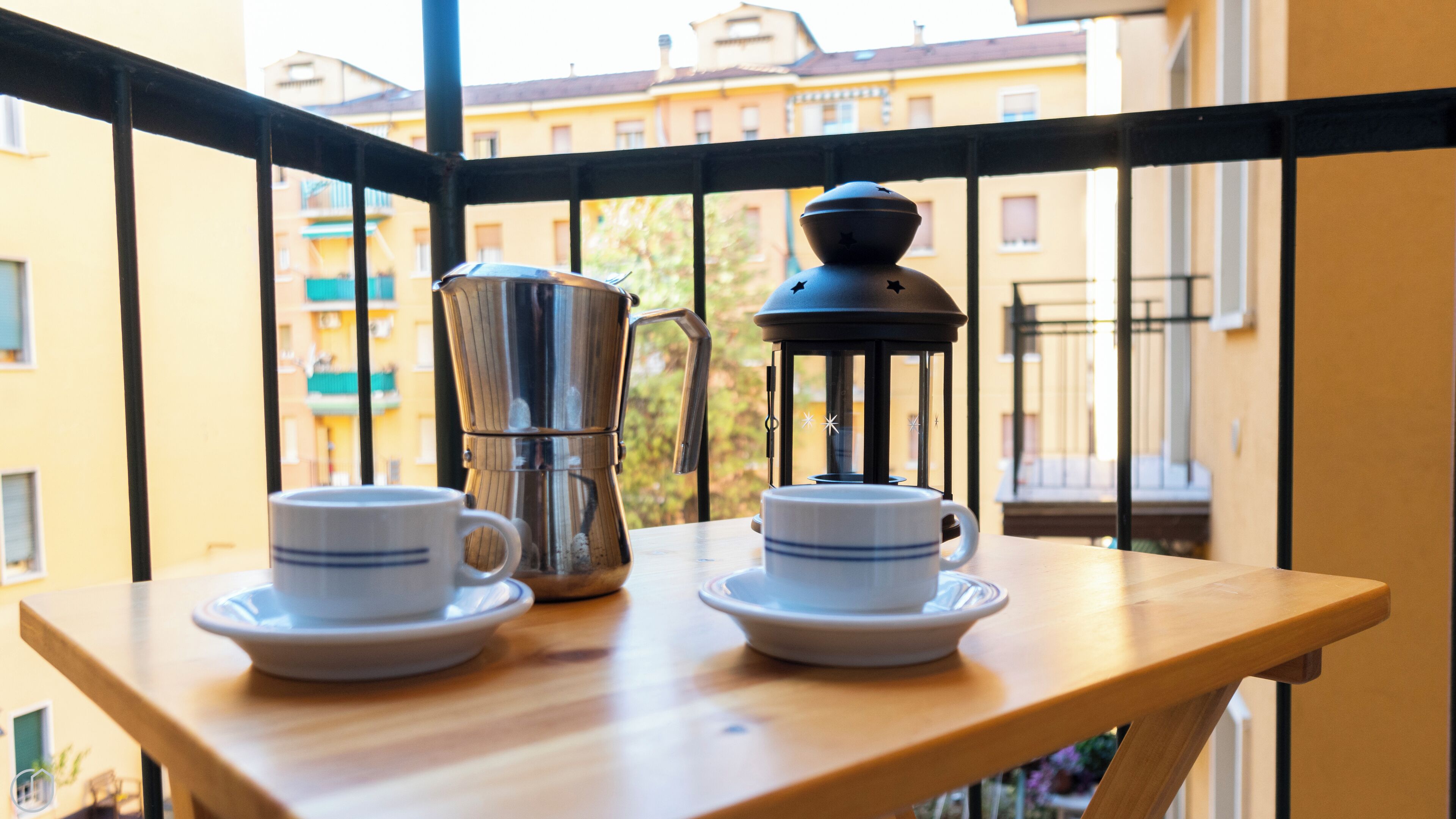 Ein Balkon mit Tisch für zwei Personen, ausgestattet mit einer Kaffeemaschine, einer Laterne und zwei Tassen mit Untertellern.