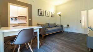 A modern living room with a sofa, a dining table, and a kitchen area visible through an open door. - Baracca 7 A - One Bedroom Apartment, Sleeps 2 (Bologna)