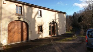 Un bâtiment doté de deux grandes portes en bois et d’une petite fenêtre, entouré d’arbres et bordé d’un chemin de terre.