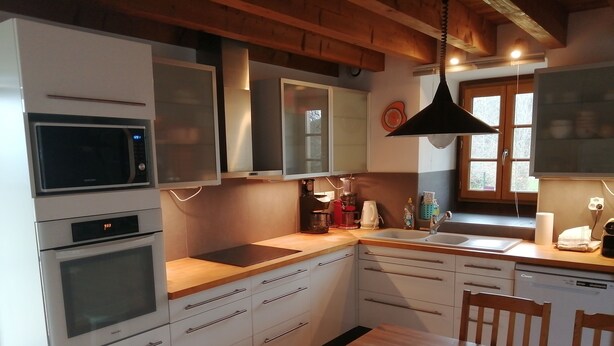 Une cuisine avec des meubles blancs, un four à micro-ondes, une cuisinière, un évier et une table à manger avec des chaises.
