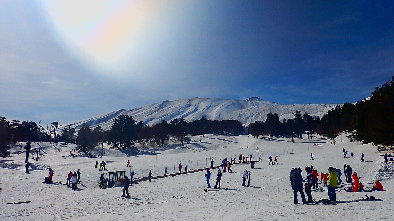Pista de esqui coberta de neve, com esquiadores e uma montanha ao fundo.