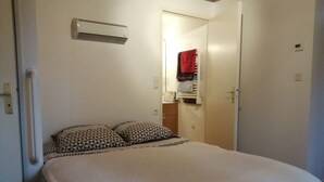Une chambre à coucher avec un lit, des oreillers, une table de chevet, un radiateur, une armoire et une porte.