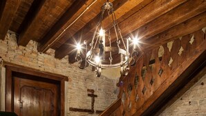 A rustic interior with a wooden staircase, a chandelier, and a stone wall.