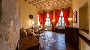 A room with wooden beams, a chandelier, red curtains, a sofa, a table, and a lamp.