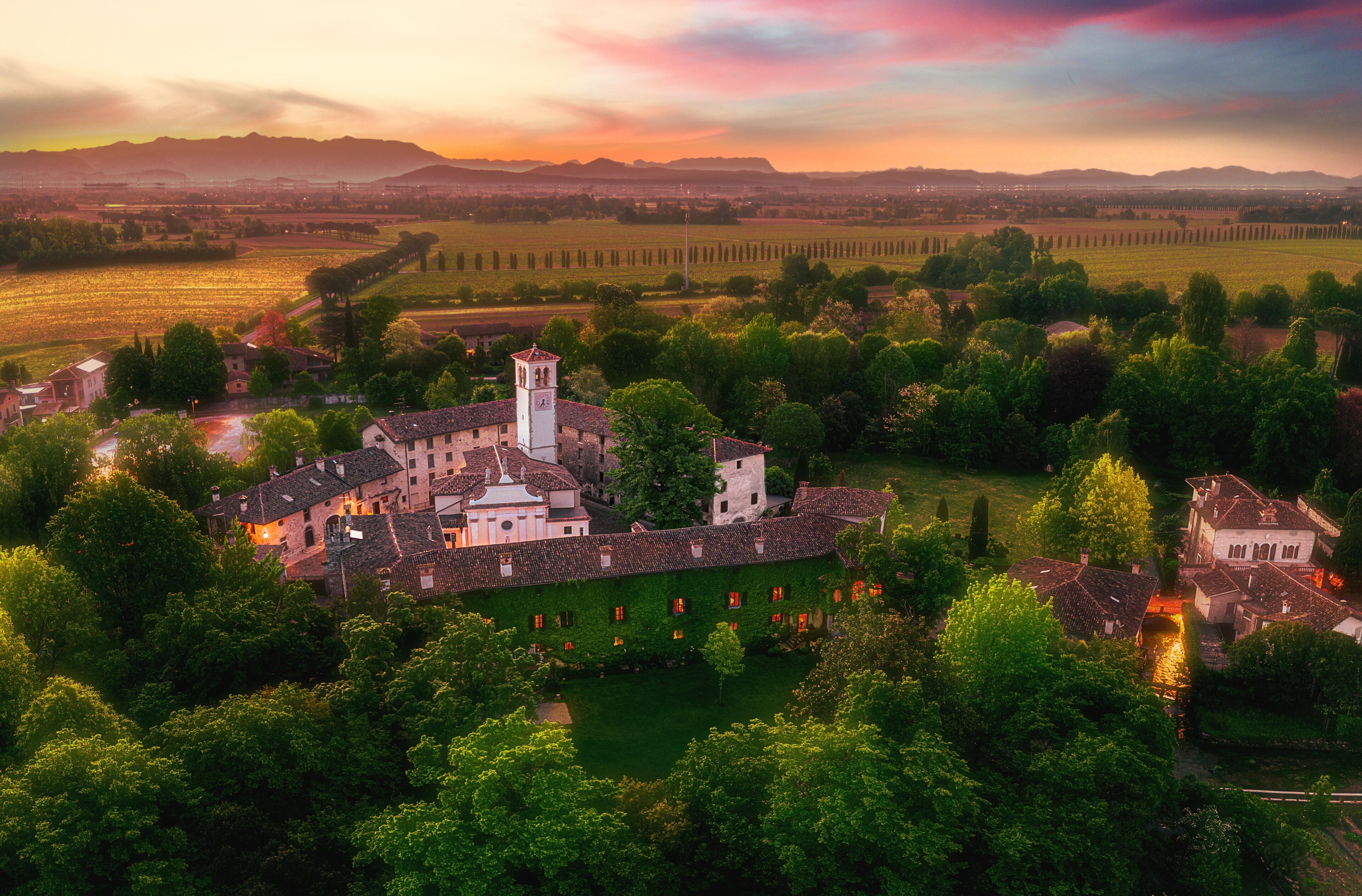 Une vue aérienne d’une ville historique, avec une église imposante au centre, entourée d’une végétation luxuriante et de champs.