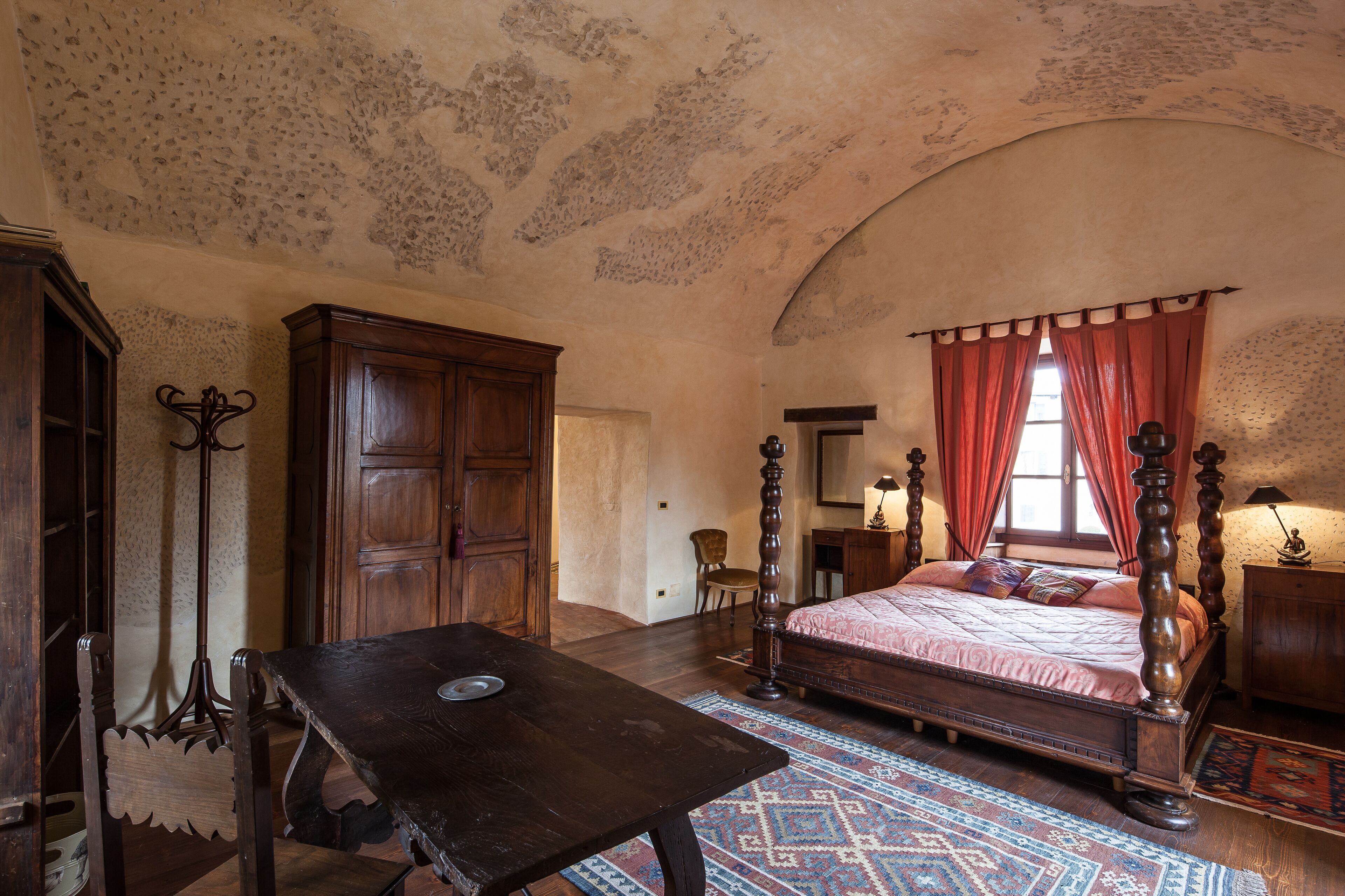 A bedroom with a four-poster bed, wooden furniture, and a patterned rug.