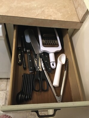 A drawer containing various kitchen utensils including a grater, scissors, and a measuring cup.
