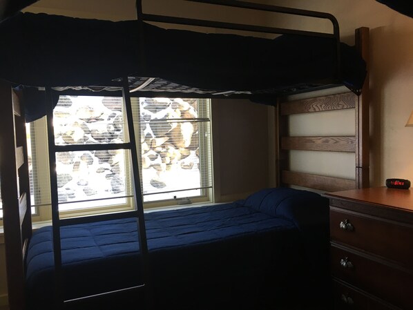 A bunk bed with a window, a dresser with drawers, and a digital clock.