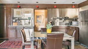 Una cucina moderna con elettrodomestici in acciaio inossidabile, un'area pranzo con un tavolo in vetro e sedie in pelle, e un tappeto decorativo sul pavimento.