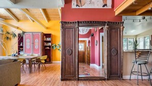 Un accogliente soggiorno con pavimento in legno, un tappeto colorato, un angolo pranzo con tavolo e sedie, e una libreria piena di libri.