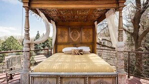 Un letto a baldacchino con struttura imponente e intagli decorativi, una testiera in legno e vista sugli alberi sullo sfondo.
