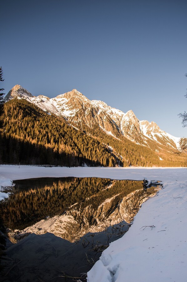 A snow-covered landscape with a lake reflecting mountains and trees. - Deluxe Apartment With Balcony and Great View (Antholz Mittertal)