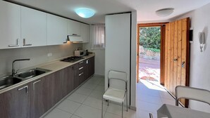 Una cocina moderna con estufa a gas, microondas y pileta de acero inoxidable. Hay una puerta de madera que da al exterior y una silla cerca de la puerta.