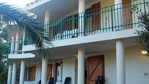 Un edificio de dos pisos con balcón, columnas y una palmera.