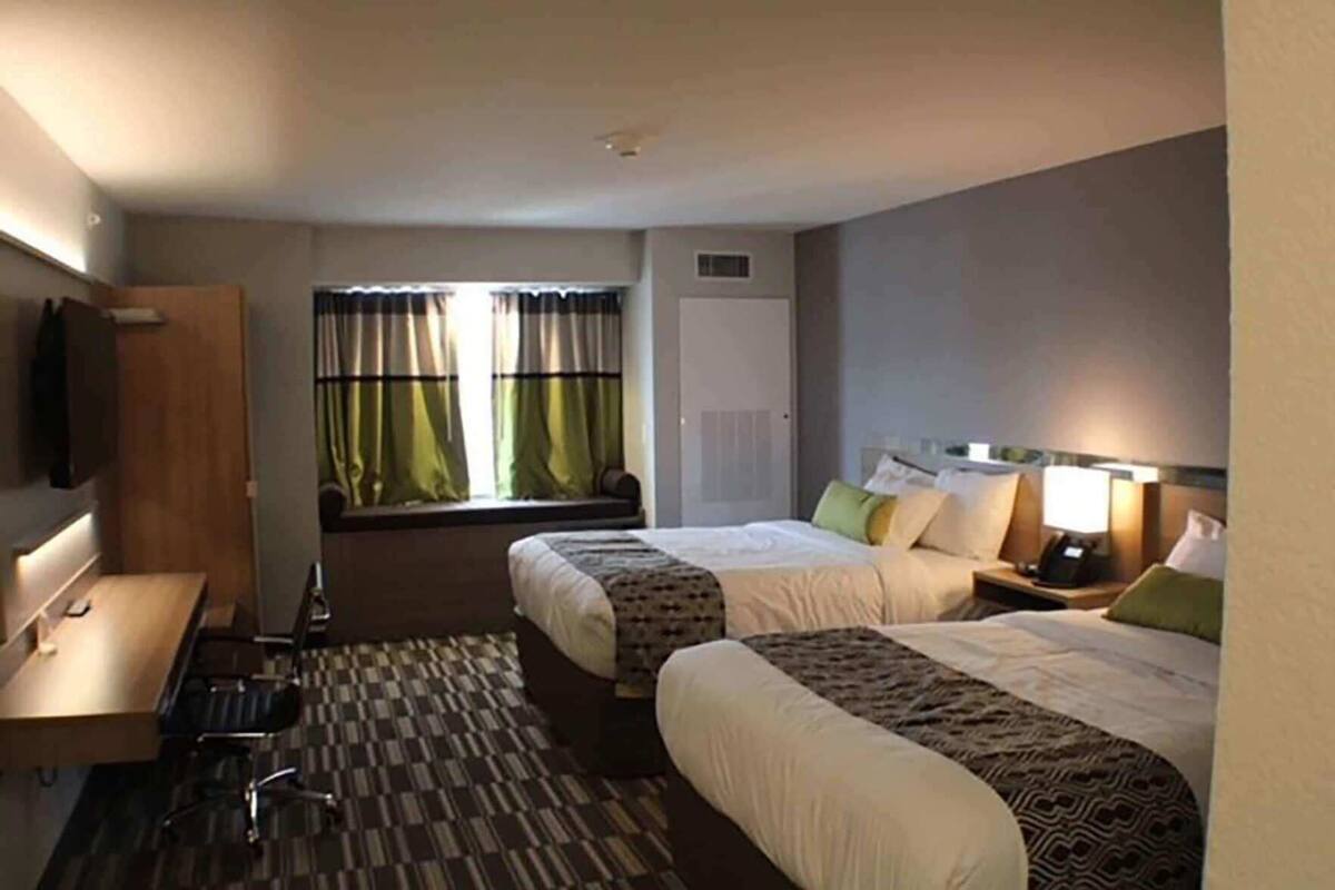 A hotel room with two beds, a desk, a chair, a TV, and a window with curtains.