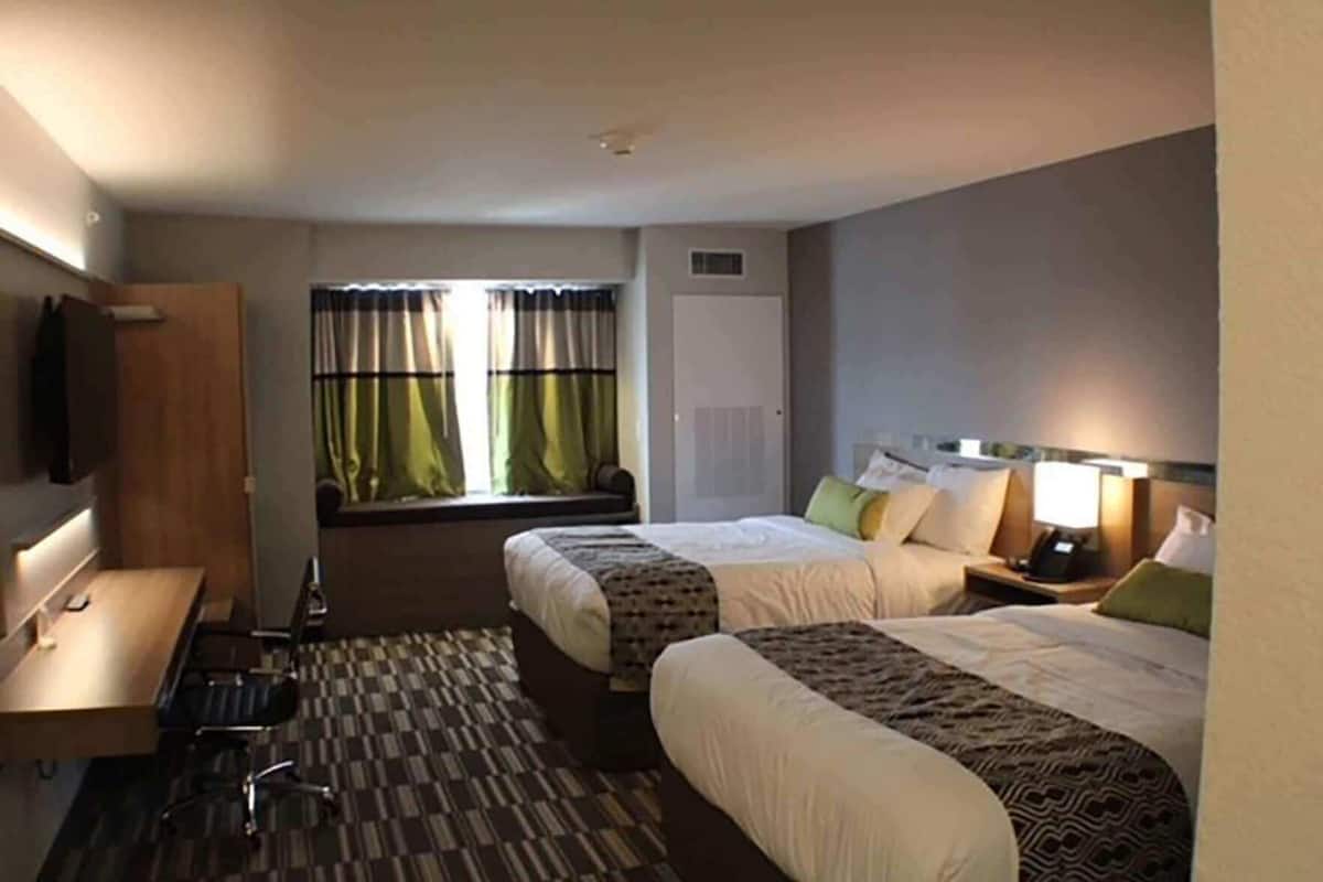 A hotel room with two beds, a desk, a chair, a TV, and a window with curtains.