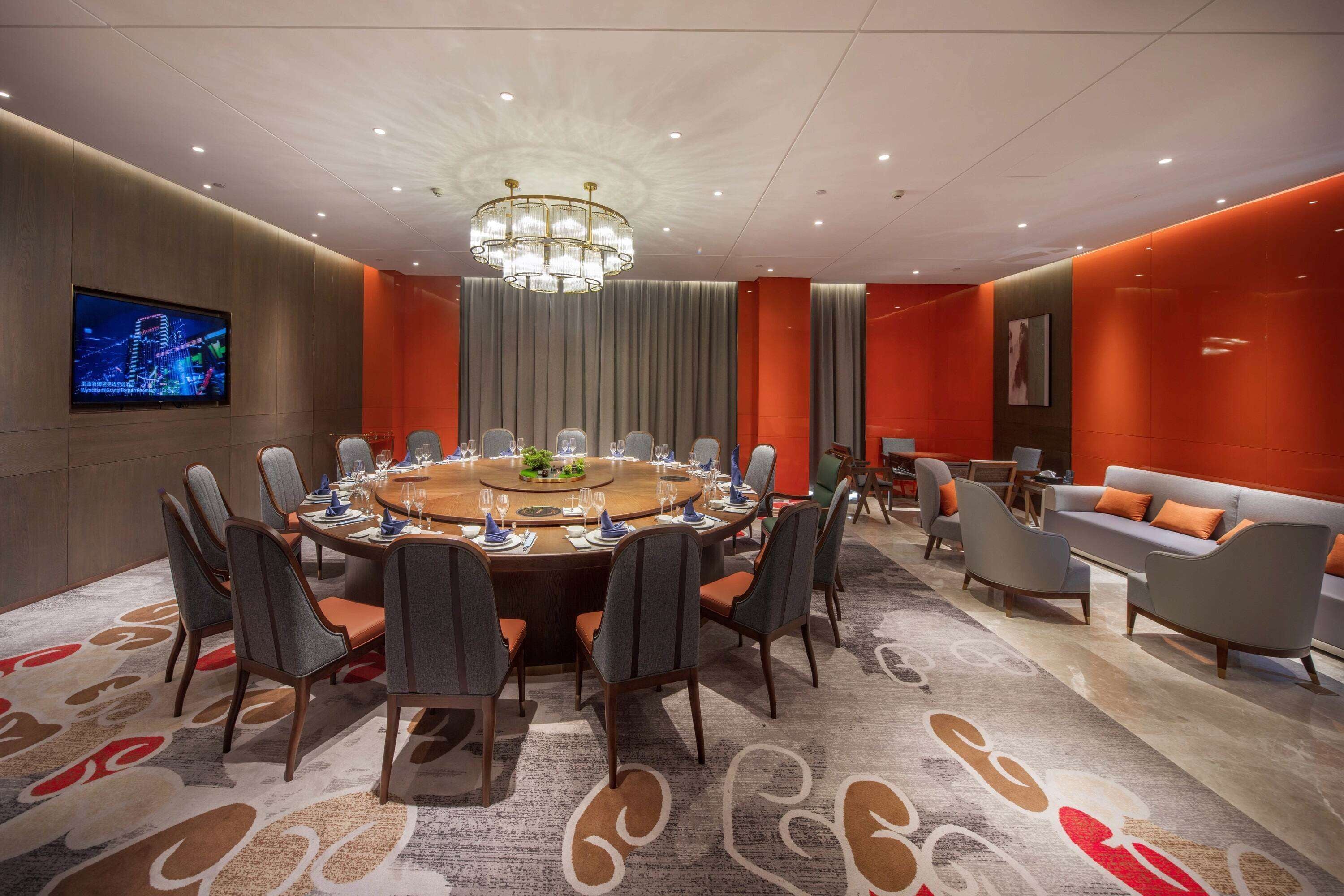 A conference room with a round table, chairs, a chandelier, a television, and a sofa.