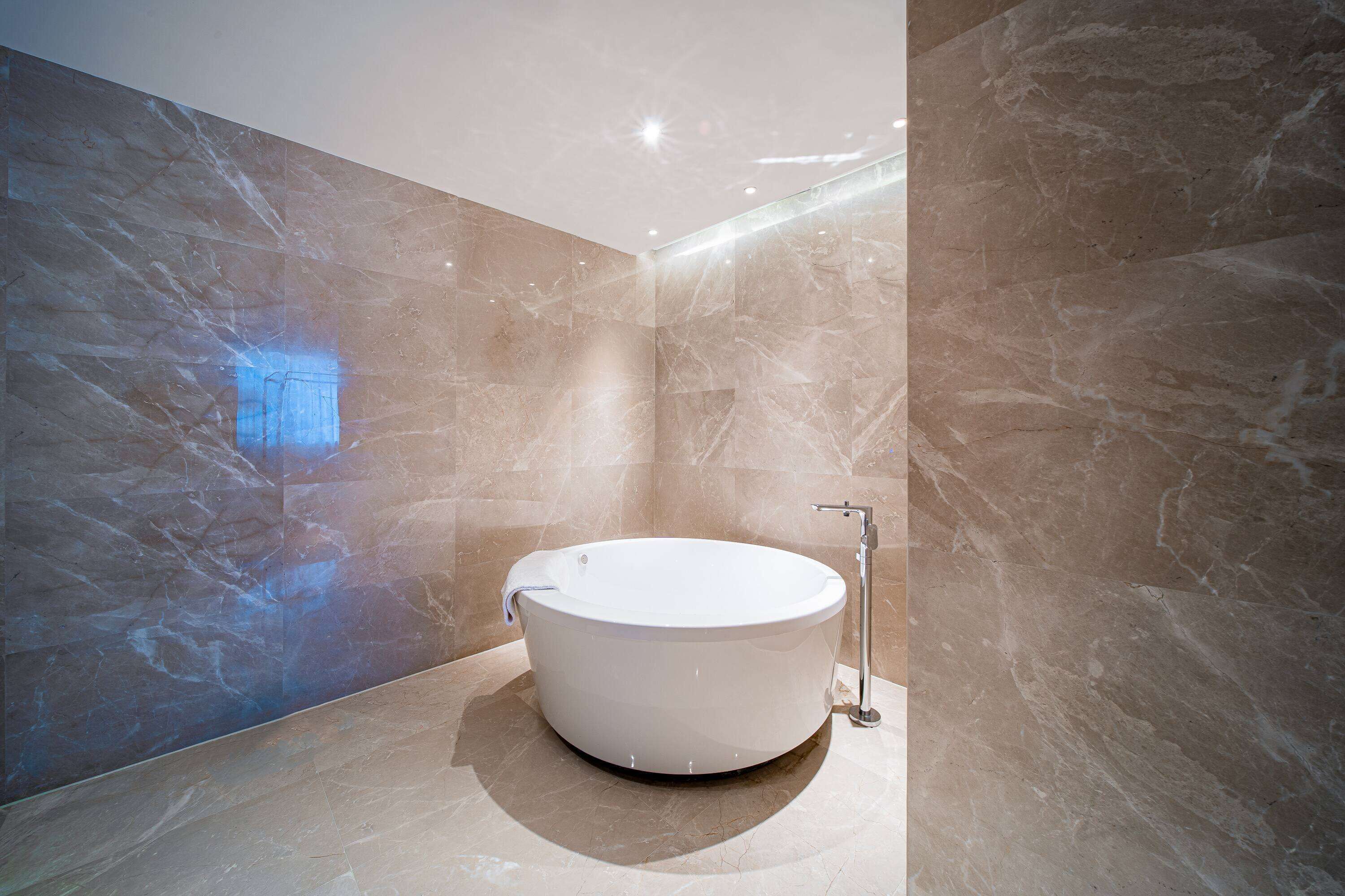 A modern bathroom with a freestanding bathtub, marble walls, and a sleek faucet.