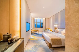 Una habitación de hotel con cama, escritorio, silla, televisor y ventana con vistas.