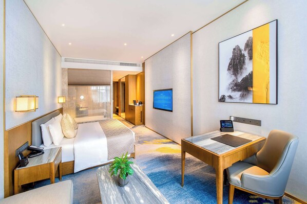 A hotel room with a bed, desk, chair, TV, and a painting on the wall.