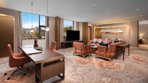 Habitación de hotel con un ventanal grande, televisor de pantalla plana, una mesa de comedor y un sofá.