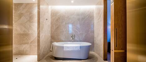 A modern bathroom with a freestanding bathtub, marble walls, and a wooden door.