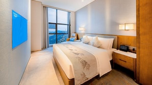 Habitación de hotel moderna con una cama grande, un televisor de pantalla plana, una mesita de noche con lámpara y vistas a la ciudad por la ventana.