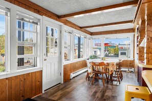 A kitchen with wooden walls and large windows, a dining table with chairs, and a yellow stool. - Whimsy Cottage - Perfect ski cottage & discounted lift tickets (North Troy)