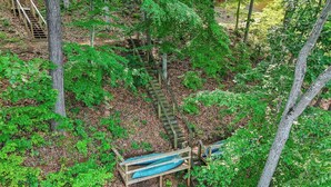 A forested area with a wooden staircase leading up and down, surrounded by dense green foliage. - Plenty of Water on the main channel. Perched on a bluff with breathtaking sunrise views over the lake, this remodeled 2BR/1BA log cabin offers memory-foam beds, well-stocked granite kitchen (farm-fresh eggs!), covered deck, stone fire pit, huge dock. (Union Hall)