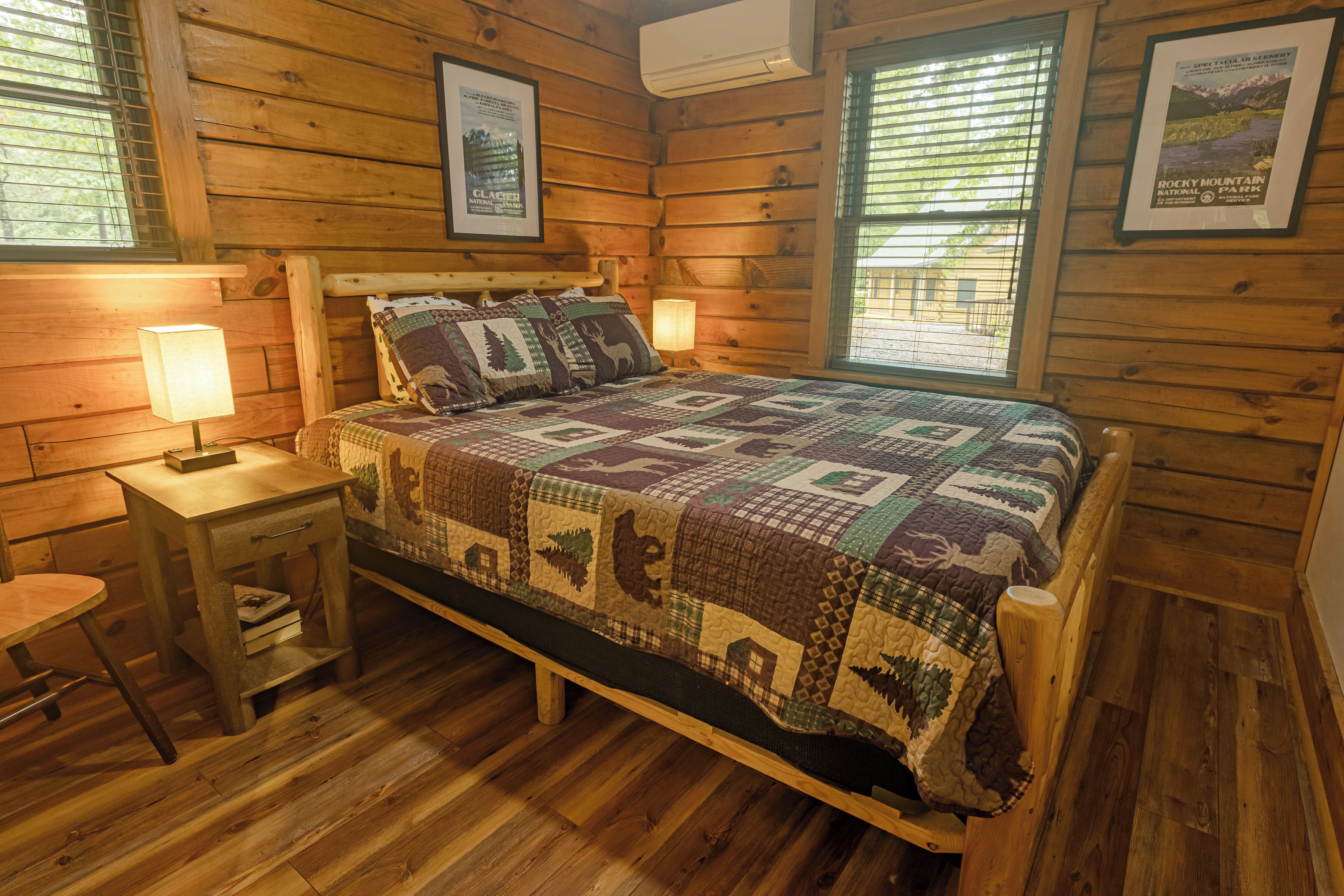 A wooden cabin bedroom with a bed, two nightstands, a lamp, and framed pictures on the walls.