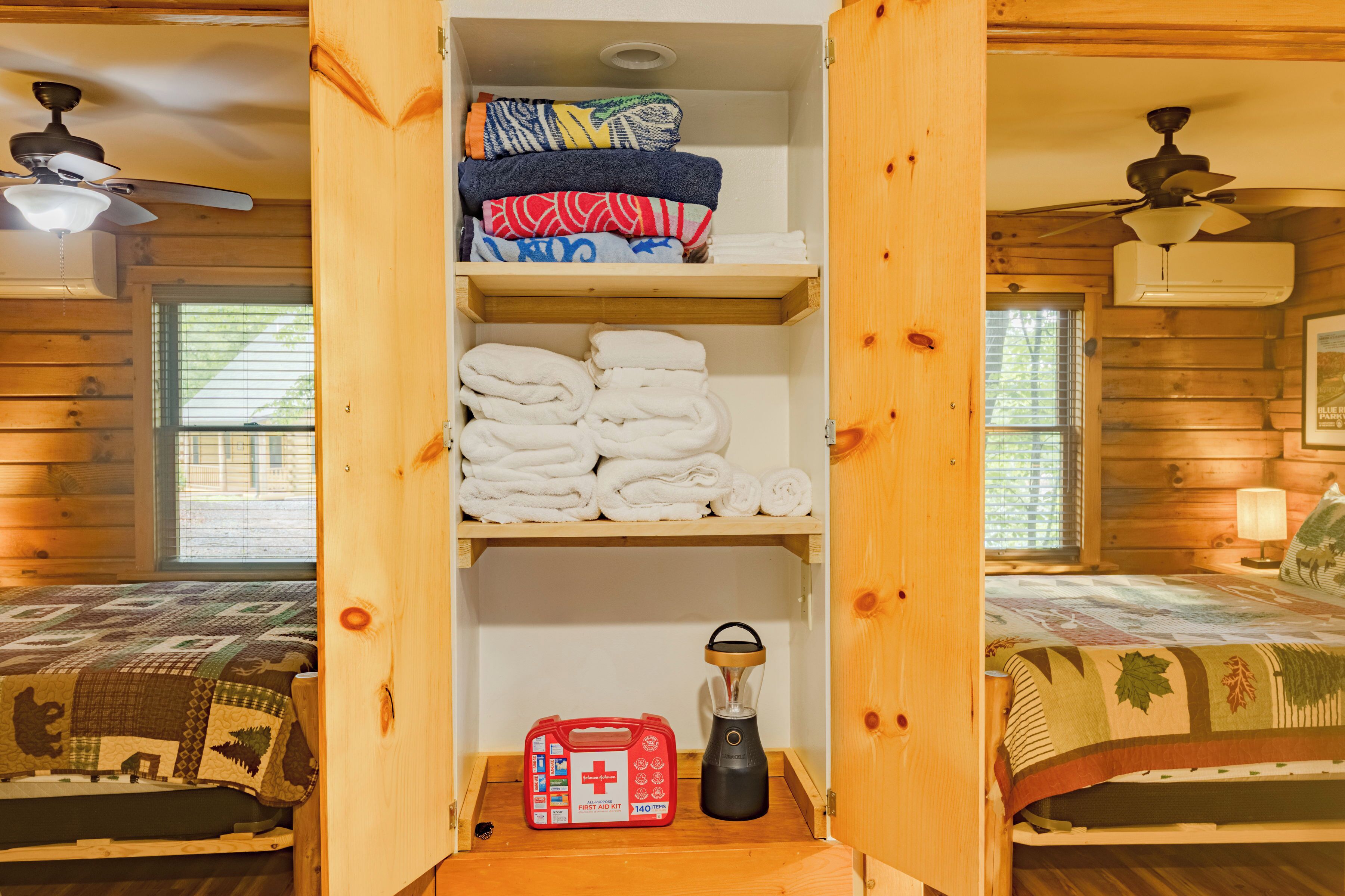A wooden cabin with two beds, a shelf with folded towels, a first aid kit, and a lantern.