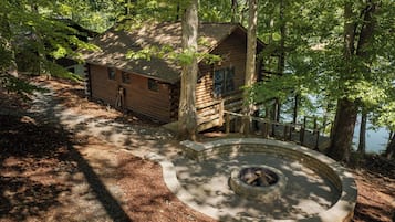 Une cabane dotée d’un foyer en pierre, entourée d’arbres et agrémentée d’une terrasse en bois.