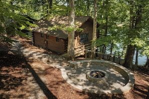 Una cabaña con un hogar de piedra, rodeada de árboles y una terraza de madera.