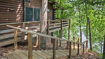 Une cabane en bois avec un escalier en bois menant à une terrasse d’où l’on peut admirer un plan d’eau.