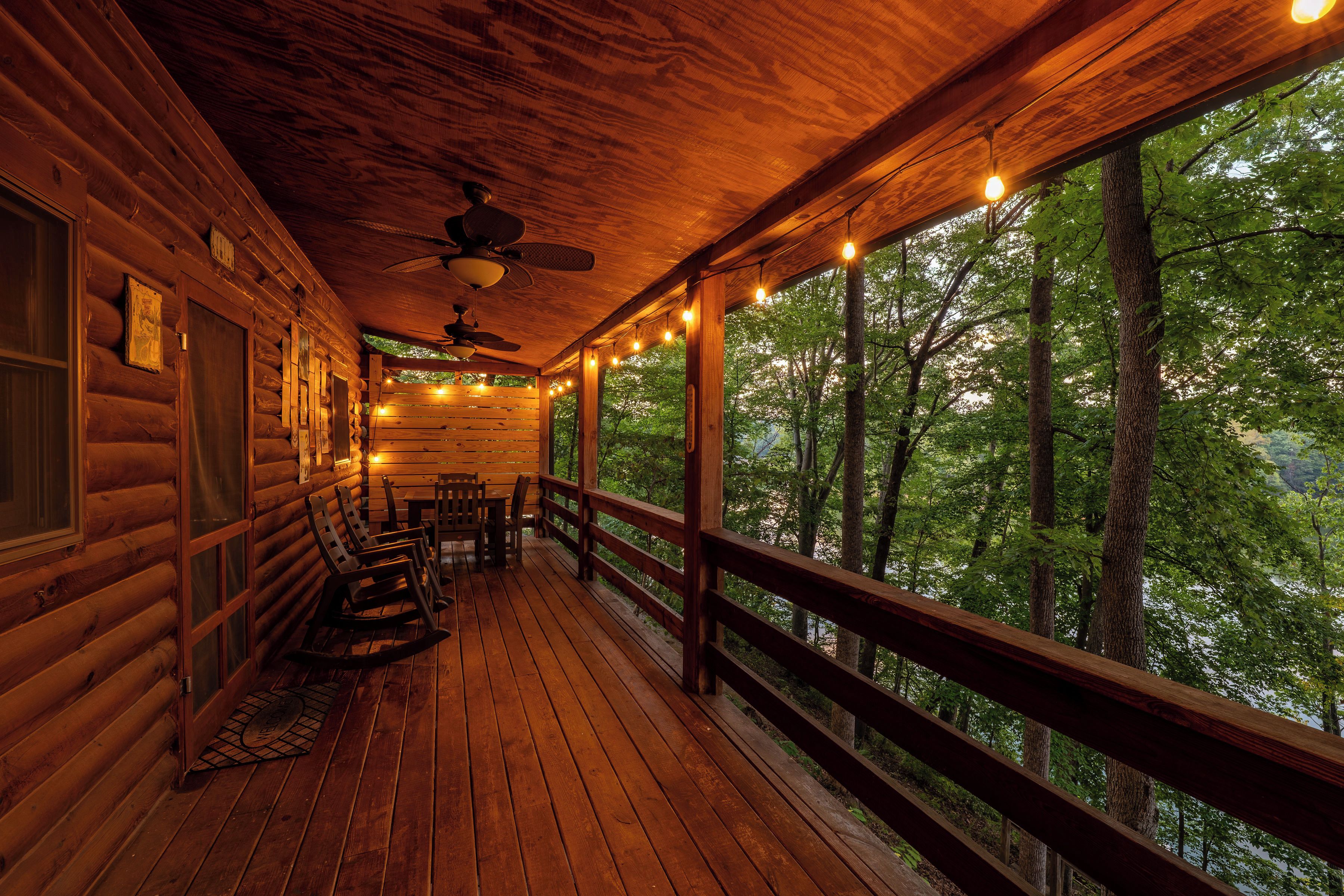 A wooden deck with rocking chairs and a table, overlooking a forested area.