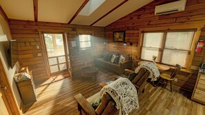 A wooden cabin interior with a sofa, chairs, a small table, and a kitchen area. - Plenty of Water on the main channel. Perched on a bluff with breathtaking sunrise views over the lake, this remodeled 2BR/1BA log cabin offers memory-foam beds, well-stocked granite kitchen (farm-fresh eggs!), covered deck, stone fire pit, huge dock. (Union Hall)