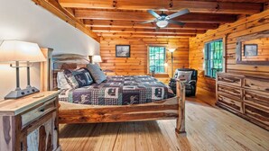 A wooden cabin bedroom with a bed, a chair, a dresser, and a ceiling fan. - Main Channel-Lots of Water-PickleBall-Hot Tubs-Fire Pits-2 Private Docks. Exclusive use of all 5 log homes, 8 acres, 1300 ft shoreline. Sleeps 36. 1400 sq ft venue, events to 75 (fee applies): weddings, reunions, retreats, milestones. 4.9★ Superhost (Union Hall)