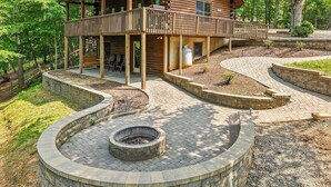 A log cabin with a deck, a fire pit, and a stone-walled patio. - Main Channel-Lots of Water-PickleBall-Hot Tubs-Fire Pits-2 Private Docks. Exclusive use of all 5 log homes, 8 acres, 1300 ft shoreline. Sleeps 36. 1400 sq ft venue, events to 75 (fee applies): weddings, reunions, retreats, milestones. 4.9★ Superhost (Union Hall)