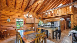 A log cabin interior with a wooden dining table, chairs, a kitchen area, and a bar. - Main Channel-Lots of Water-PickleBall-Hot Tubs-Fire Pits-2 Private Docks. Exclusive use of all 5 log homes, 8 acres, 1300 ft shoreline. Sleeps 36. 1400 sq ft venue, events to 75 (fee applies): weddings, reunions, retreats, milestones. 4.9★ Superhost (Union Hall)