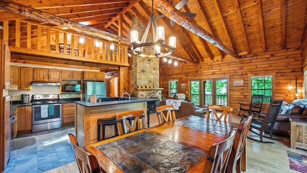 A spacious log cabin interior with a large dining area, kitchen, and a cozy living room. - Main Channel-Lots of Water-PickleBall-Hot Tubs-Fire Pits-2 Private Docks. Exclusive use of all 5 log homes, 8 acres, 1300 ft shoreline. Sleeps 36. 1400 sq ft venue, events to 75 (fee applies): weddings, reunions, retreats, milestones. 4.9★ Superhost (Union Hall)