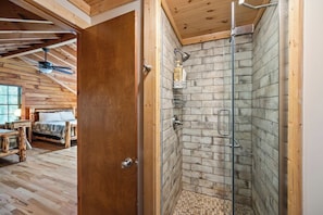 Un interior de madera con zona de ducha, cama y ventilador de techo.