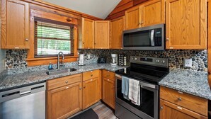 A kitchen with wooden cabinets, a granite countertop, a microwave, a stove, and a dishwasher.