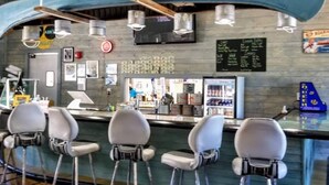 A bar area with a counter, bar stools, hanging lights, a refrigerator, and a chalkboard menu.