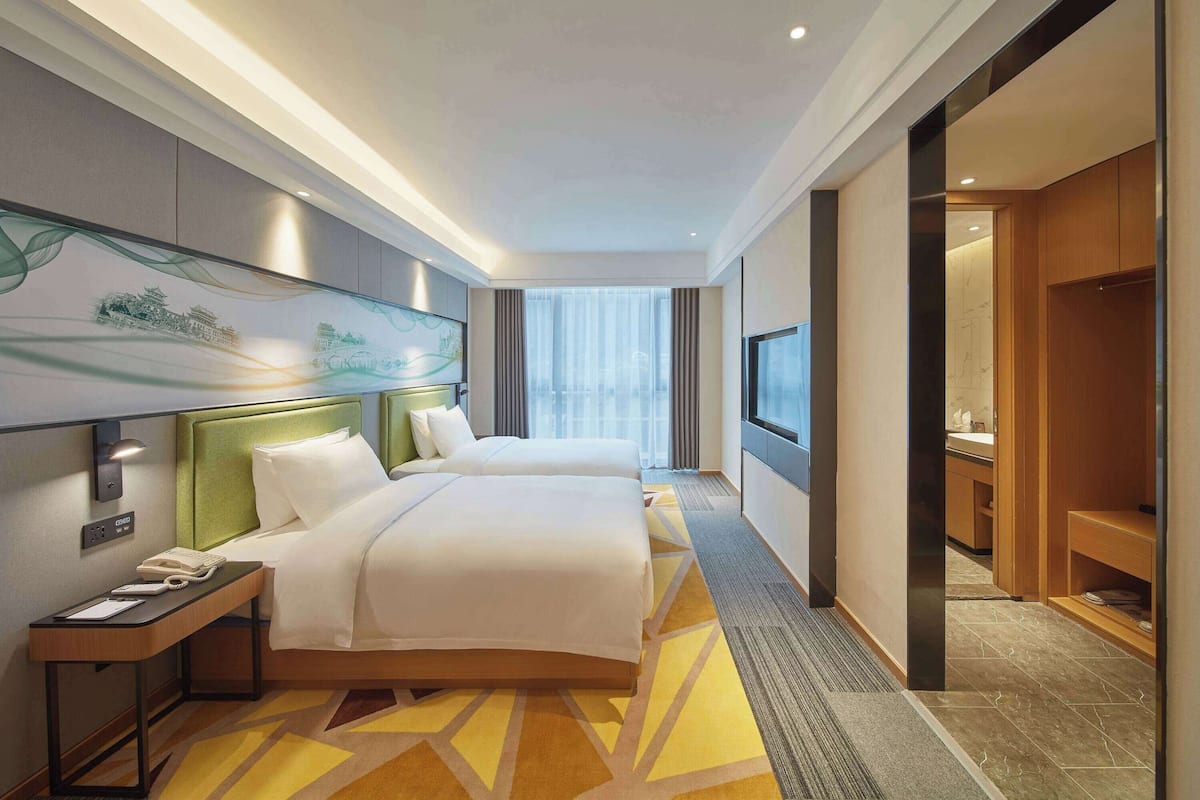 A hotel room with two beds, a desk with a telephone, a TV, and a large window with curtains.