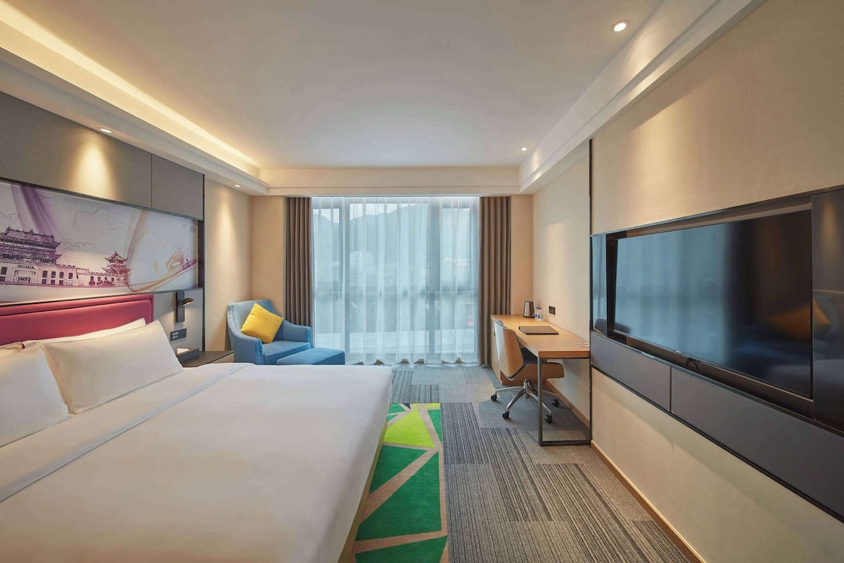 A hotel room with a large bed, a desk, a TV, and a window with curtains.