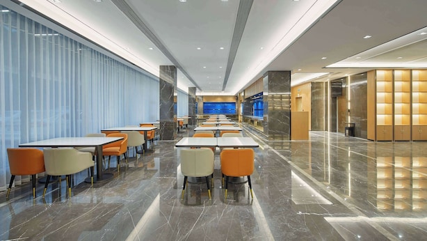 Un hall d’hôtel moderne avec un long comptoir d’accueil, plusieurs espaces de détente avec des tables et des chaises, et un sol en marbre poli.