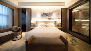 A modern hotel room with a large bed, a sofa, a small table, and a large artwork on the wall. - Ramada Plaza by Wyndham Hezhou North (Hezhou)